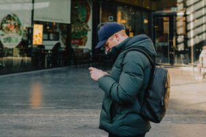 Man in coat uses phone outside a building.